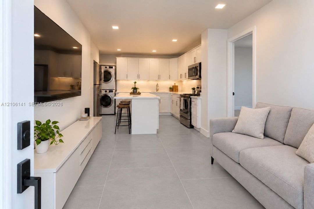 Open-concept interior featuring large-format tile flooring, recessed lighting, white shaker-style cabinetry, stainless steel appliances, and a central kitchen island