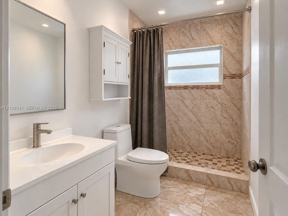 Bathroom featuring a vanity with a white countertop and undermount sink, wall-mounted medicine cabinet, walk-in shower with tiled surround and stone-finish floor, and neutral tile flooring
