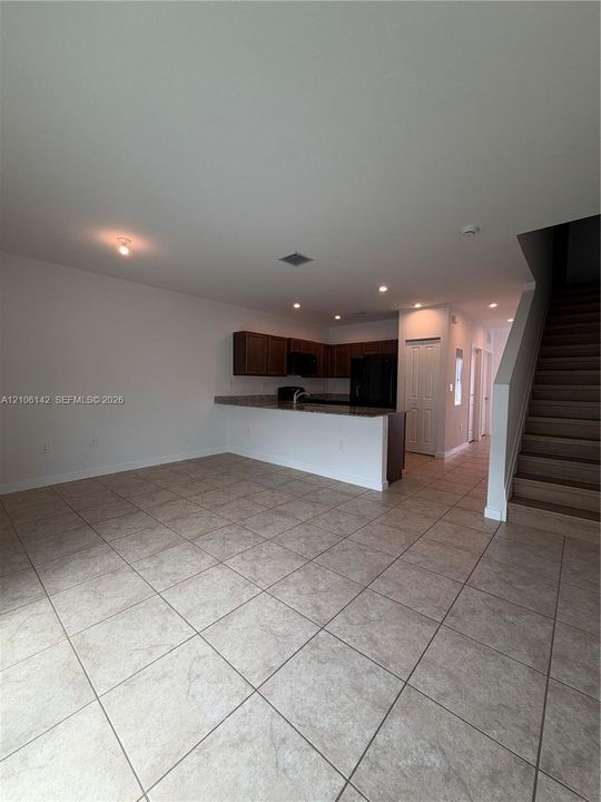 Open-concept interior featuring large-format ceramic tile flooring, a kitchen breakfast bar, stone-finish countertops, dark wood-finish cabinetry, and a carpeted staircase