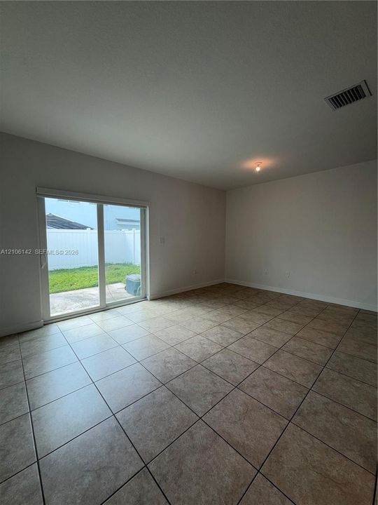 Neutral interior space featuring ceramic tile flooring, sliding glass patio doors, and exterior access to a concrete patio and fenced yard
