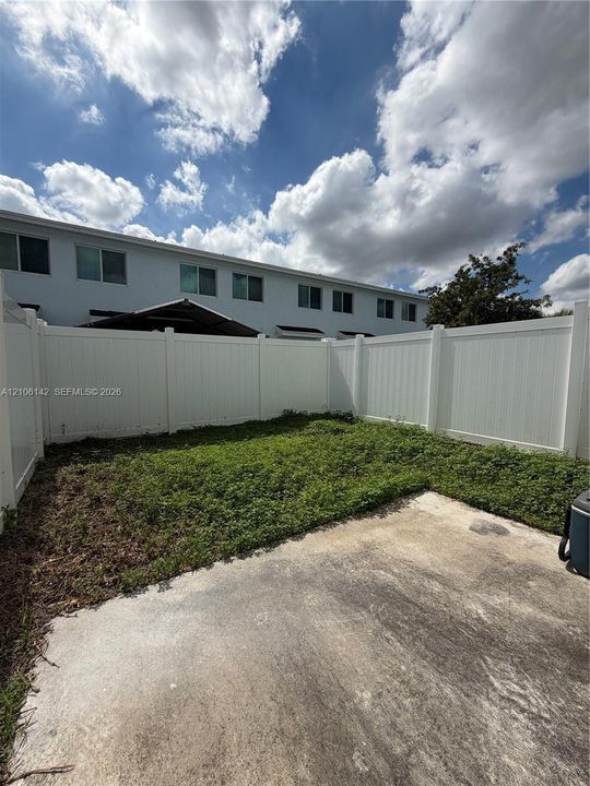Private backyard area featuring a concrete patio, grassy lawn, and tall white vinyl privacy fencing