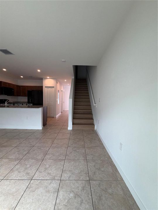 Open-concept interior featuring large-format tile flooring, recessed lighting, and a staircase with a handrail
