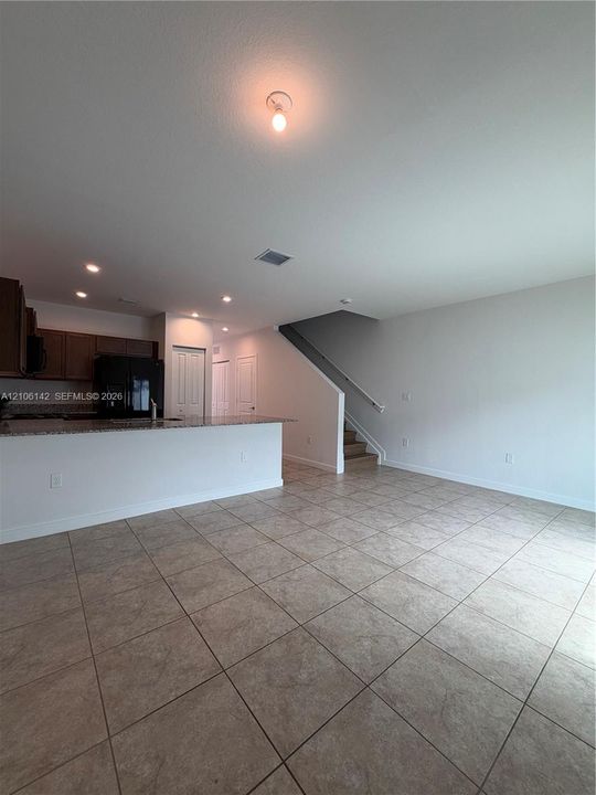 Large-format ceramic tile flooring, kitchen featuring a stone-composite countertop, dark wood-finish cabinetry, built-in staircase with a railing, and recessed ceiling lighting