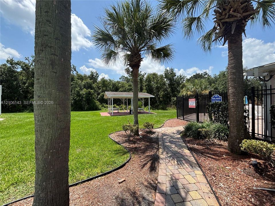 Paver walkway featuring mature palm trees, manicured lawn, and a covered open-air structure