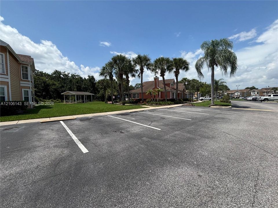 Asphalt parking lot featuring marked stalls, a manicured lawn, a covered gazebo, and mature palm trees