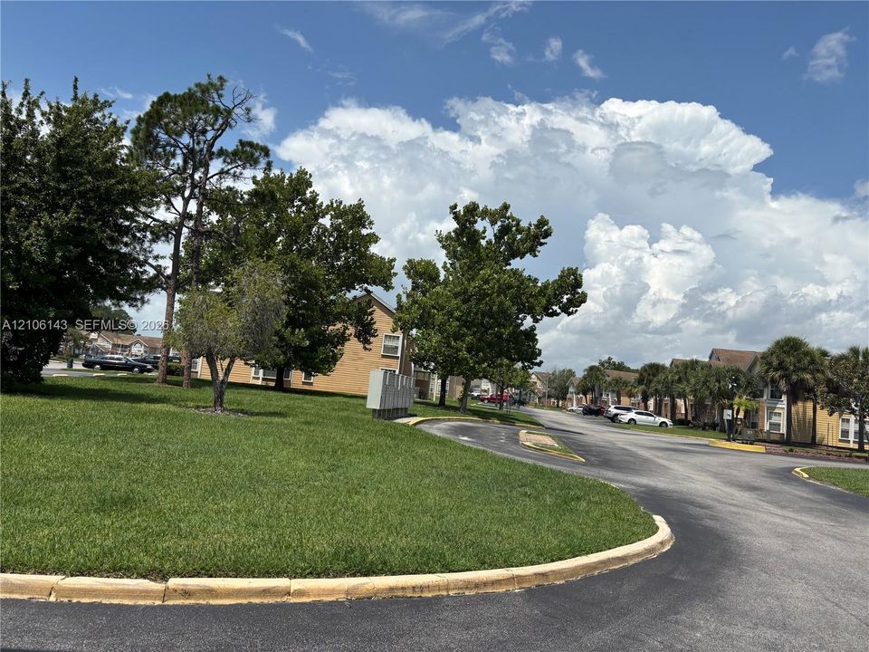 Landscaped common grounds featuring mature trees, expansive manicured lawn areas, and asphalt access roads