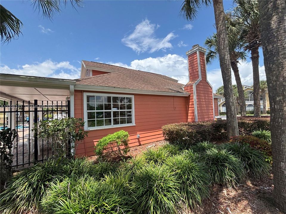 Exterior featuring shingle and horizontal siding, a prominent brick chimney, multi-pane windows, an attached covered patio, and metal perimeter fencing