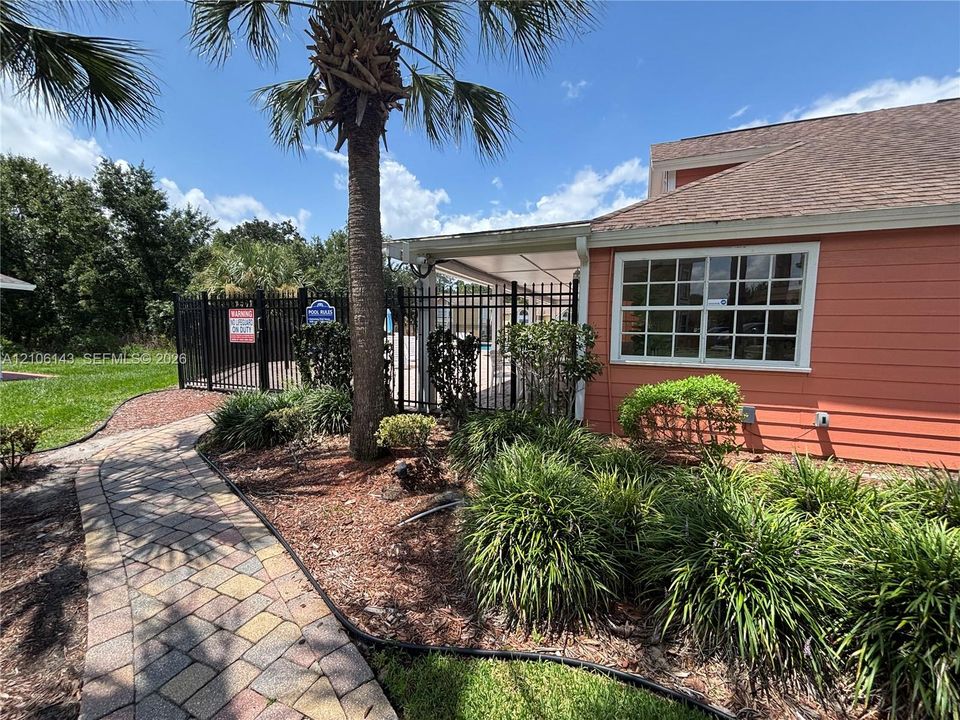 Exterior featuring horizontal siding, multi-pane windows, a paver walkway, mature landscaping, and a metal perimeter fence