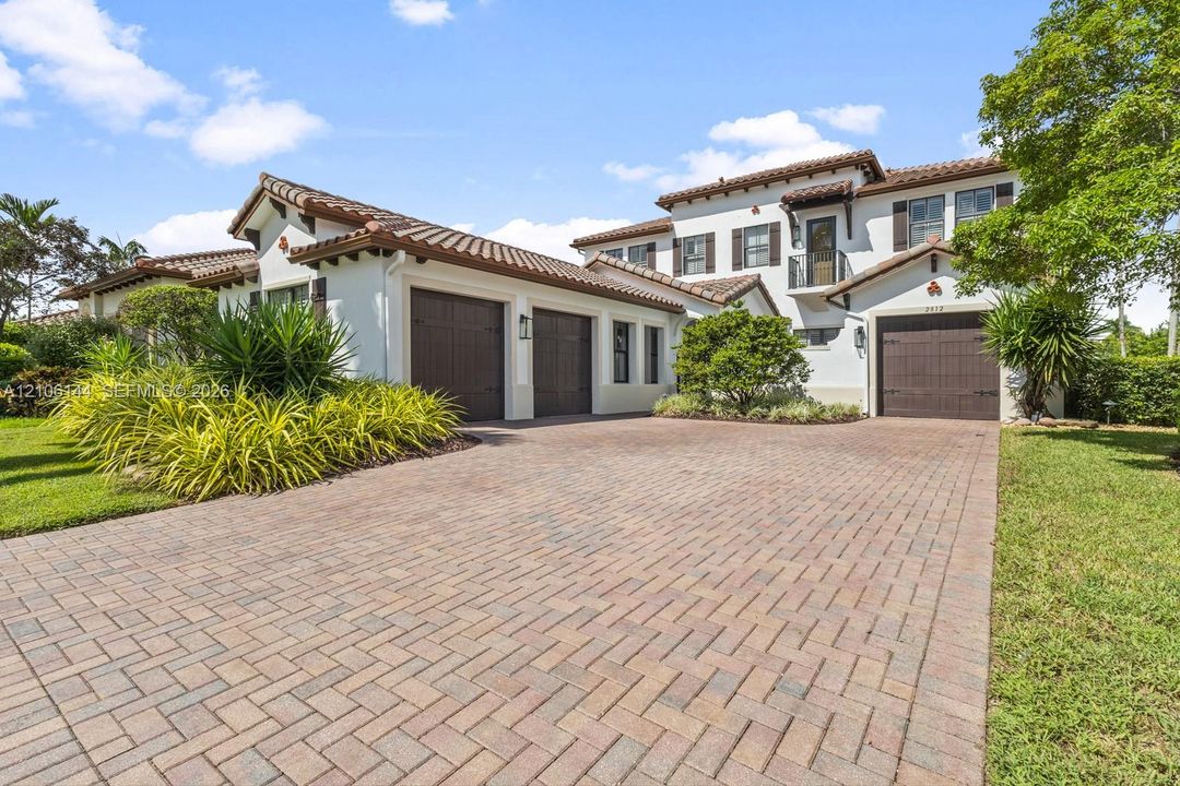 Mediterranean-style exterior featuring stucco siding, a multi-car garage with wood-finish doors, a paver driveway, and a tile roof