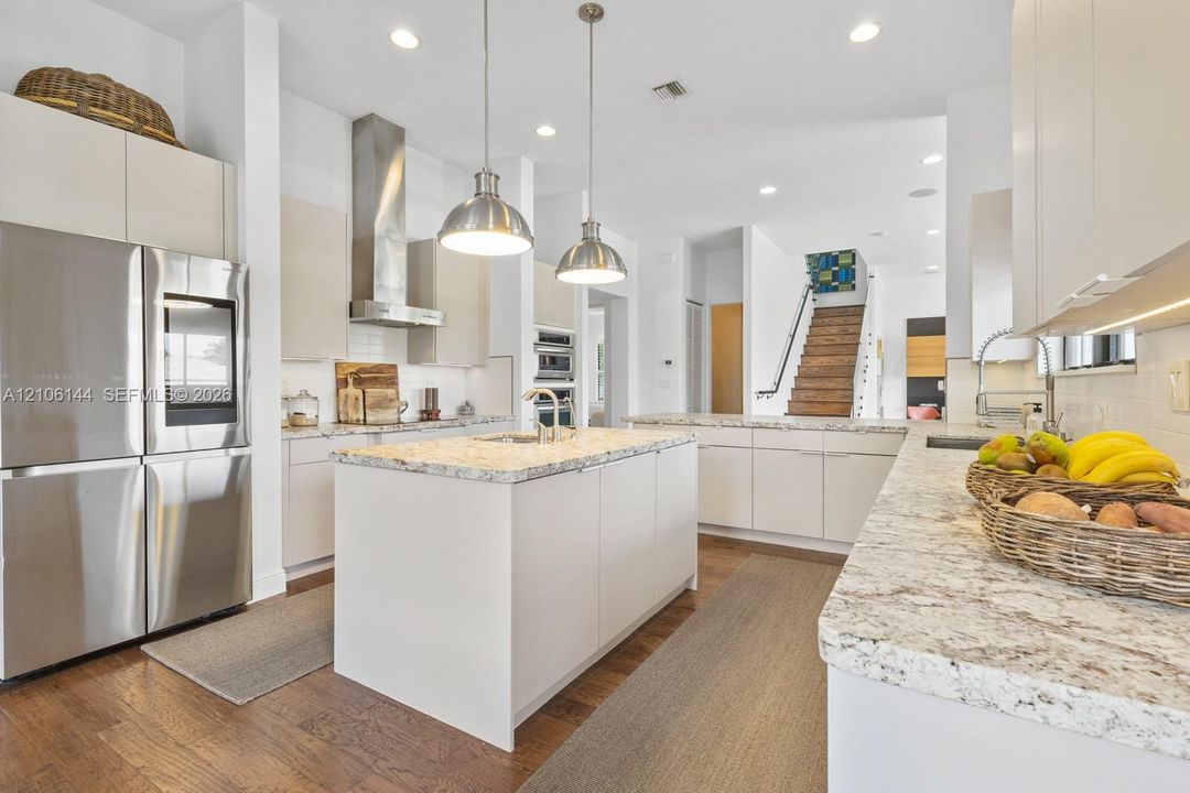 Kitchen featuring a central island with stone-style countertops, stainless steel appliances, flat-panel cabinetry, and pendant lighting over wood-finish flooring