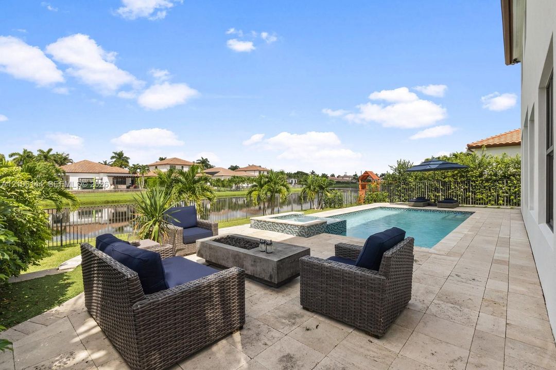 Backyard featuring a stone paver patio, swimming pool with a raised spa, and metal perimeter fencing
