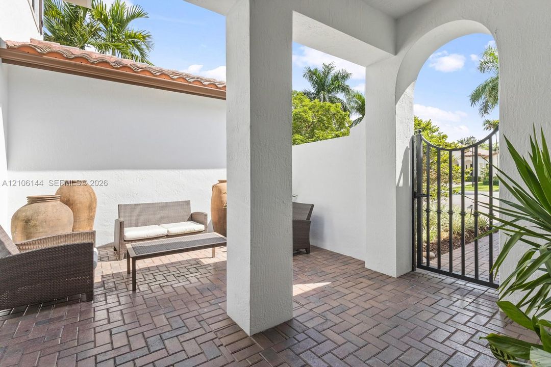Covered courtyard featuring herringbone-pattern brick flooring, stucco walls, arched entryway, and a decorative wrought-iron gate