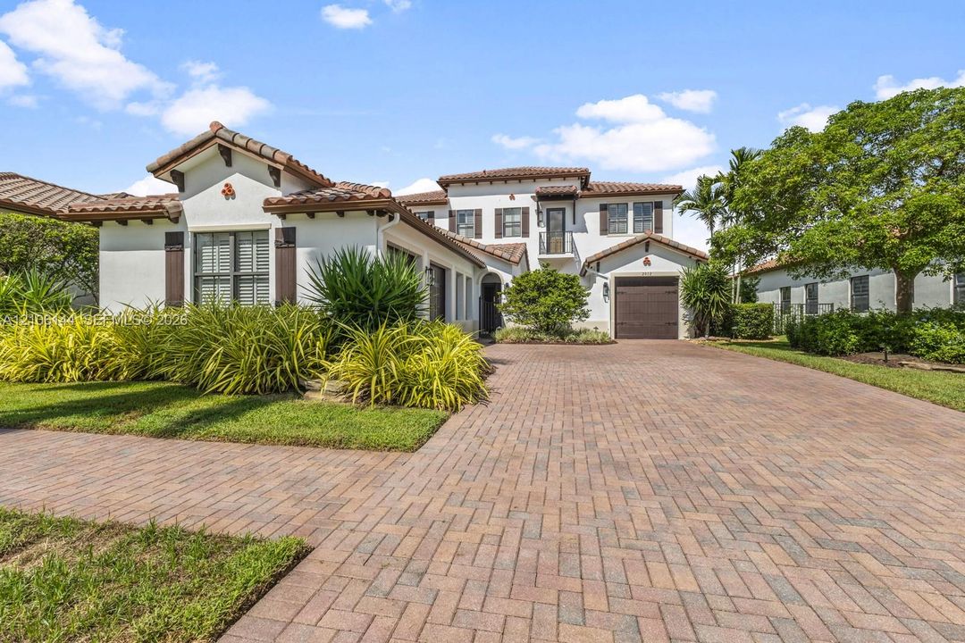 Mediterranean-style exterior featuring a clay tile roof, stucco facade, decorative shutters, a paved herringbone driveway, and a second-level wrought iron balcony