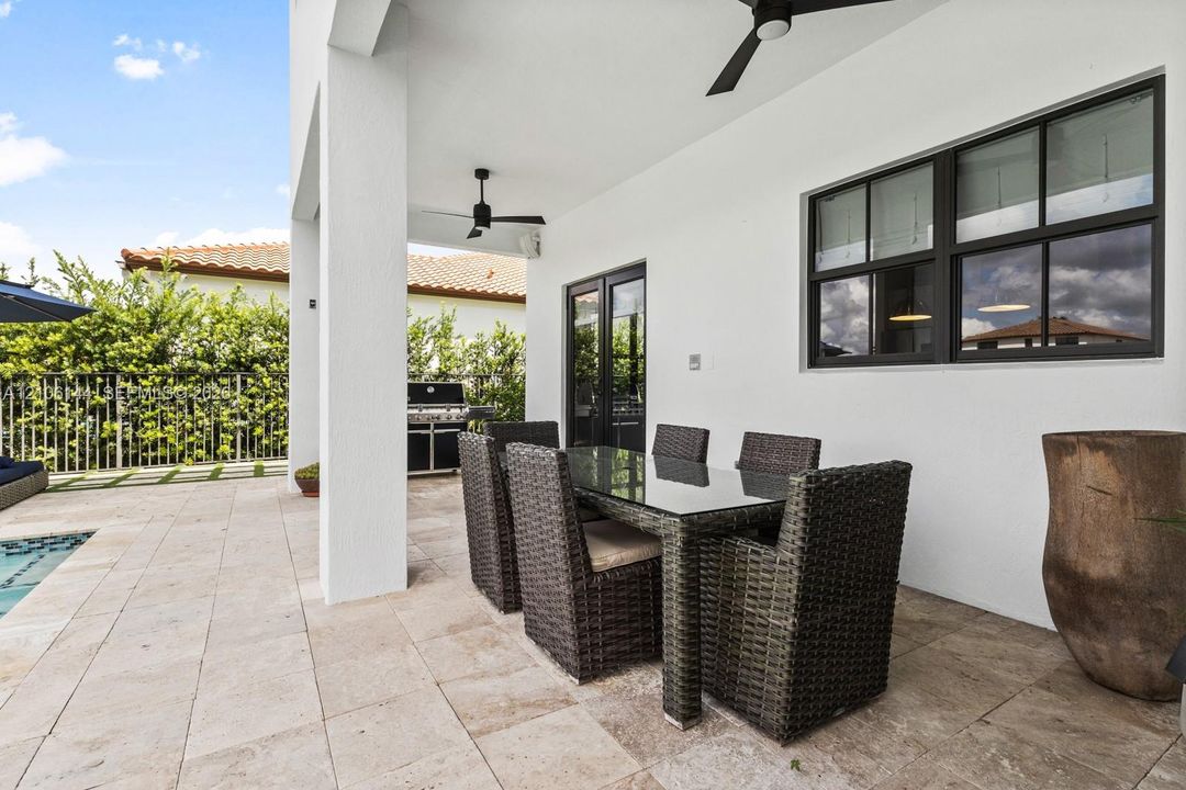 Covered patio featuring stone tile flooring, black-framed windows, and ceiling-mounted fans