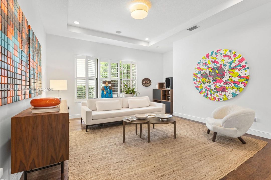 Living area featuring a tray ceiling, recessed lighting, wood-finish flooring, and plantation shutters