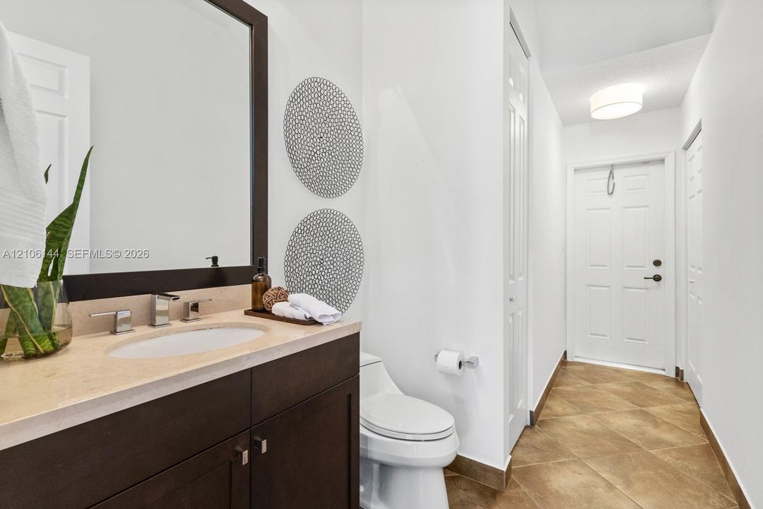 Dark wood vanity with a stone countertop, oval undermount sink, matching framed mirror, and tile flooring