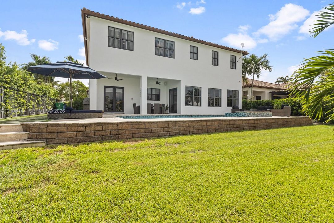 Two-story stucco exterior with a tile roof, featuring a covered patio, a raised stone retaining wall, and an integrated swimming pool