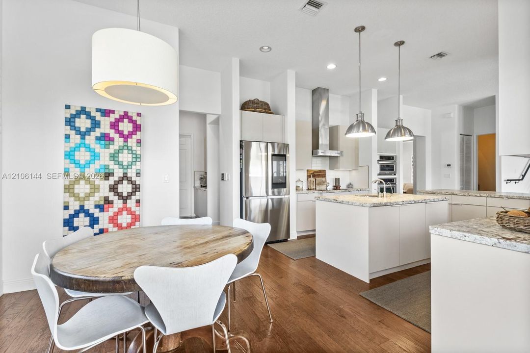 Kitchen featuring an island with stone-finish countertops, stainless steel appliances, a stainless steel range hood, built-in wall ovens, and wood-finish flooring