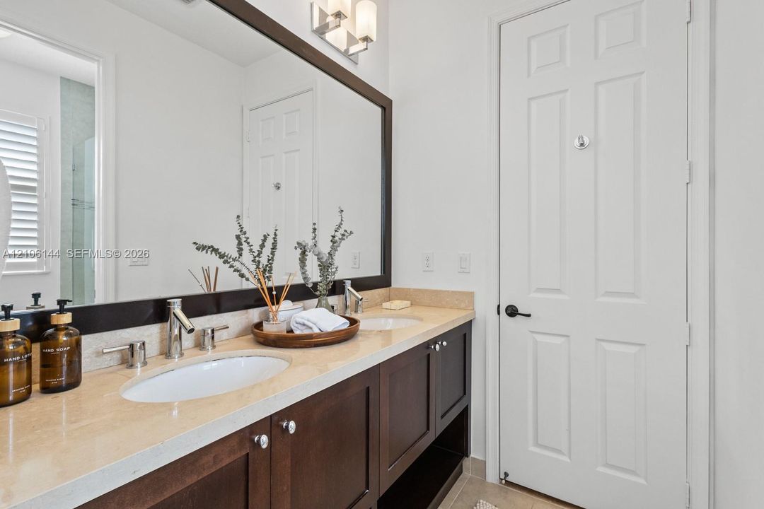 Dual-sink vanity featuring dark wood cabinetry, a light-toned solid surface countertop, large framed wall mirror, and modern chrome fixtures