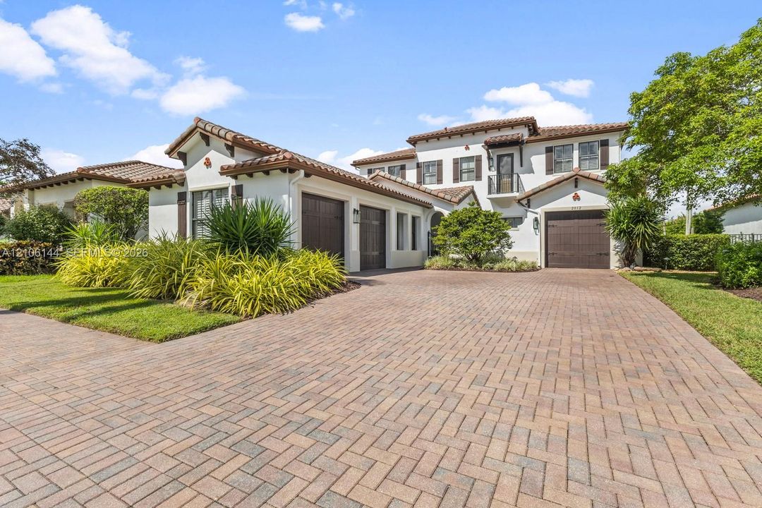 Mediterranean-style architecture featuring a tile roof, stucco exterior, paved herringbone driveway, three-car garage, and a second-story balcony
