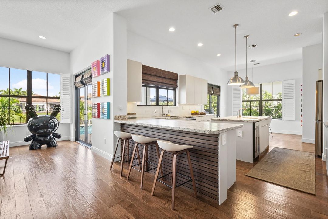 Kitchen featuring wood-finish flooring, a horizontal slat-paneled island, stone-surfaced countertops, recessed lighting, and metal pendant fixtures