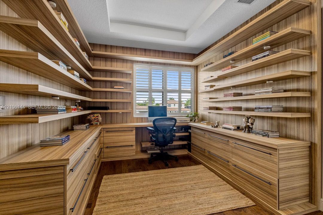 Custom-built wood-veneer cabinetry with extensive integrated shelving, deep-drawer storage, a coordinated built-in desk, and plantation shutters