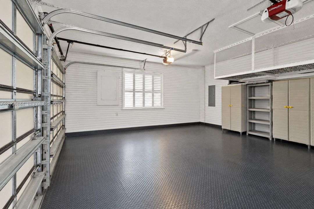 Finished garage featuring textured floor coating, horizontal slat wall paneling, ceiling-mounted storage rack, and built-in floor-to-ceiling storage cabinetry