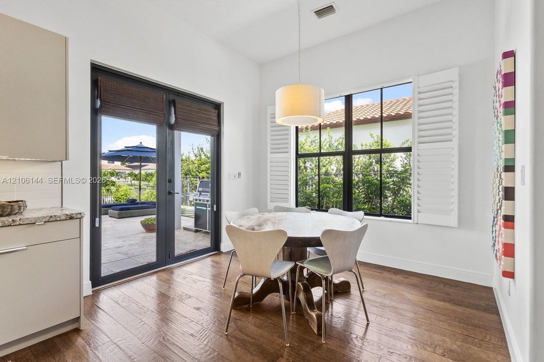 Dining area featuring wood-finish flooring, double glass doors with dark framing, multi-pane windows with white plantation shutters, and a drum-style pendant light fixture