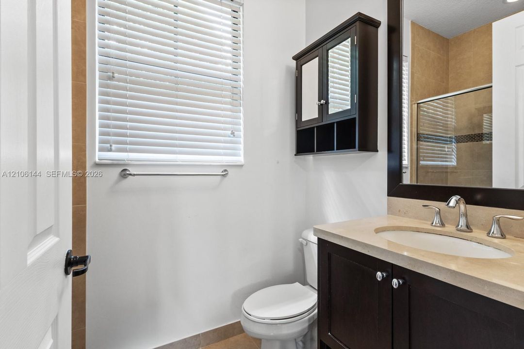 Dark wood-finish vanity with a stone countertop, integrated undermount sink, matching wall-mounted storage cabinet, and tiled flooring