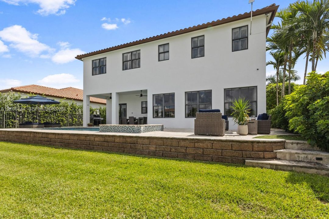 Two-story exterior featuring white stucco finish, a covered patio, a raised stone retaining wall, and an integrated pool and spa with mosaic tile accents