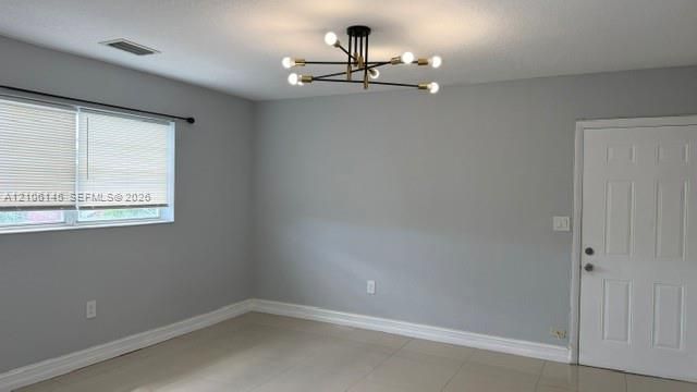 Neutral-toned interior space featuring large-format tile flooring, multi-light modern chandelier, and six-panel door