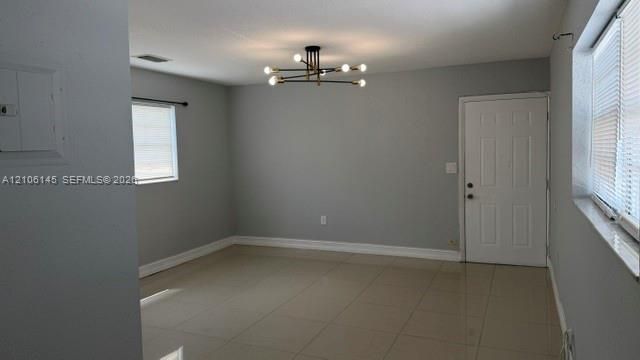 Interior space featuring large-format neutral tile flooring, modern multi-arm chandelier, six-panel door, and windows fitted with horizontal blinds