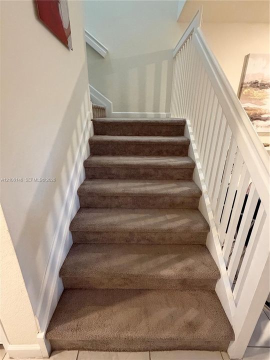 Staircase featuring wall-to-wall carpeting, white wooden balusters, and a painted handrail