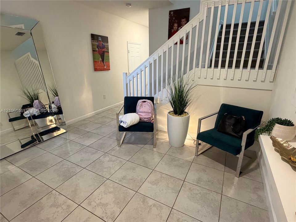 Neutral tile flooring, staircase with white wooden balusters, and a wall-mounted flush-mount light fixture