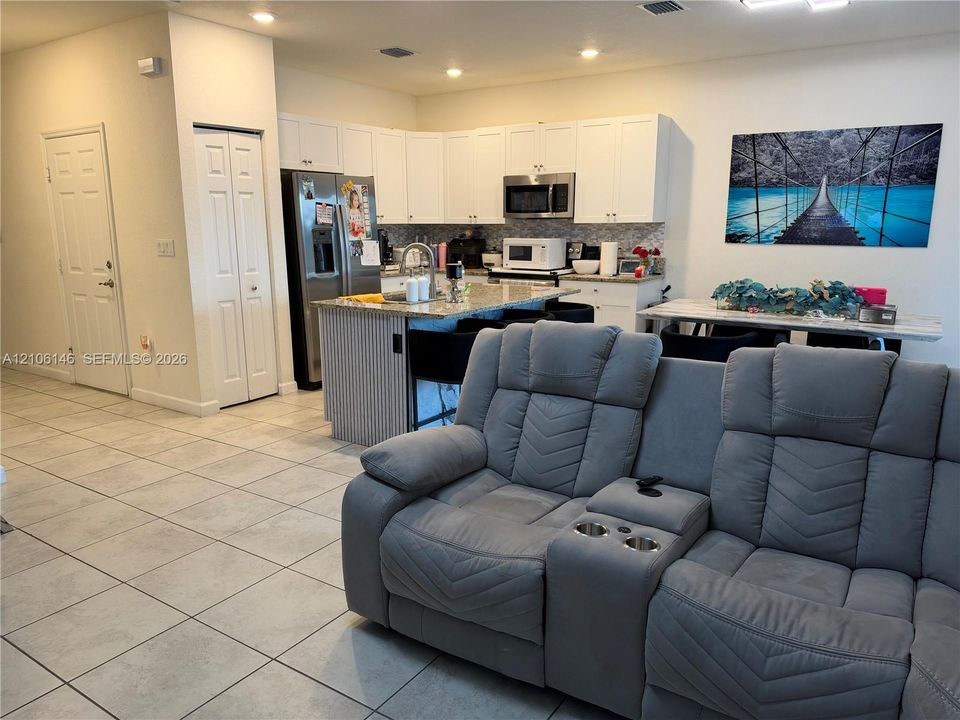 Kitchen featuring white shaker-style cabinetry, stone-finish countertops, a central island with a fluted detail finish, stainless steel appliances, and large-format ceramic tile flooring