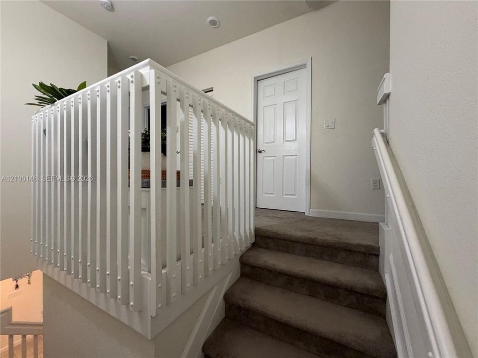 White vertical-slat stair railing with a matching handrail and carpeted staircase featuring a six-panel door