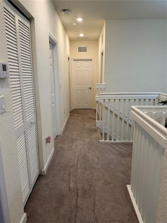 Hallway featuring neutral wall-to-wall carpeting, white louvered-door closet, recessed ceiling lighting, and white wooden balustrade
