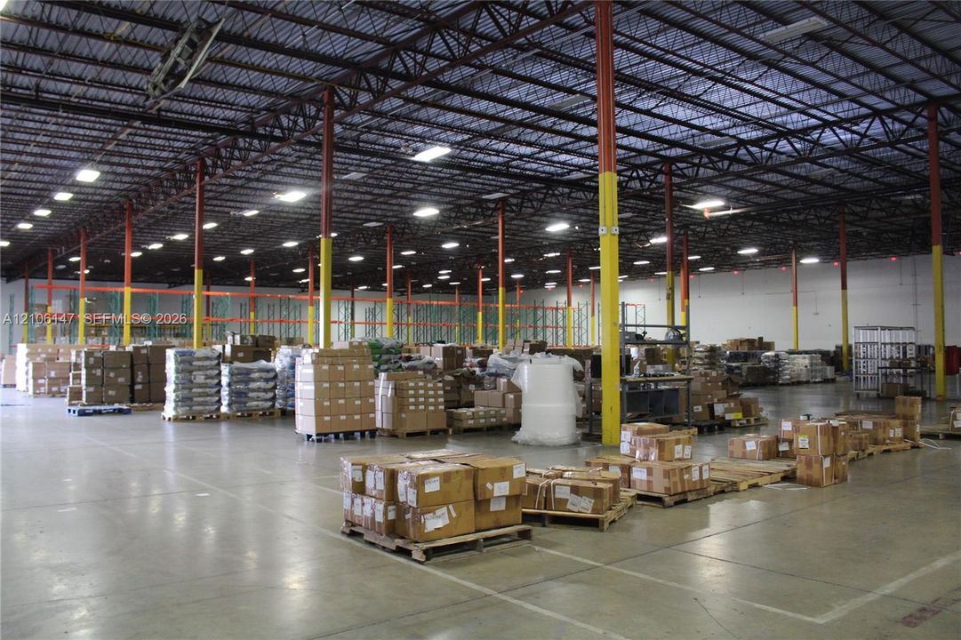 Industrial warehouse facility featuring high-clearance exposed steel truss ceilings, polished concrete flooring, extensive overhead LED lighting, and structural support columns
