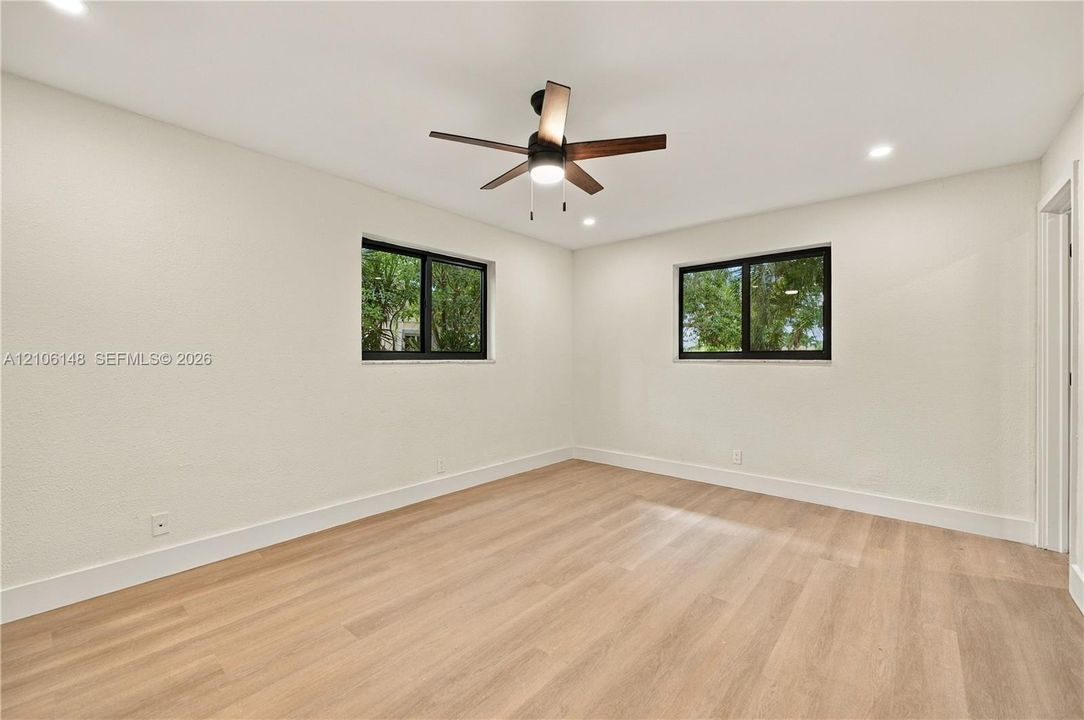 Neutral interior space featuring wood-finish flooring, recessed lighting, a ceiling fan with integrated lighting, and dual windows with black frames