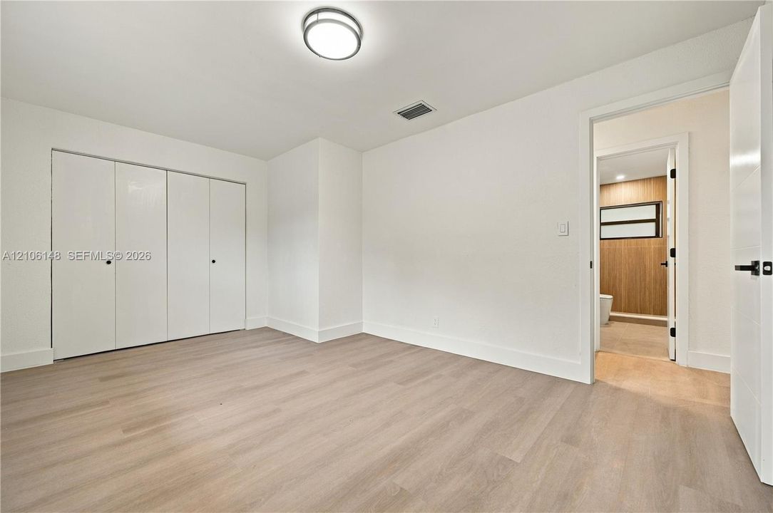 Interior room featuring wood-finish flooring, white walls, flush-mount lighting, and floor-to-ceiling closets with double-door access