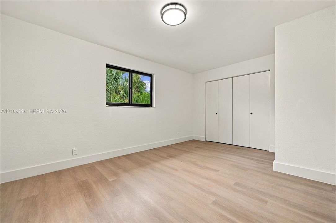 Neutral-toned wood-finish flooring, white walls, dual-panel closet doors, single-hung window with black frame, and flush-mount ceiling lighting