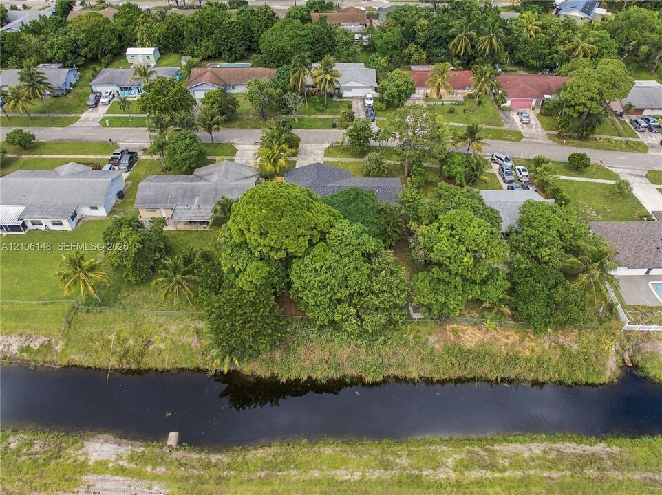 Aerial perspective featuring a waterfront lot, mature trees, and a residential structure with an asphalt shingle roof