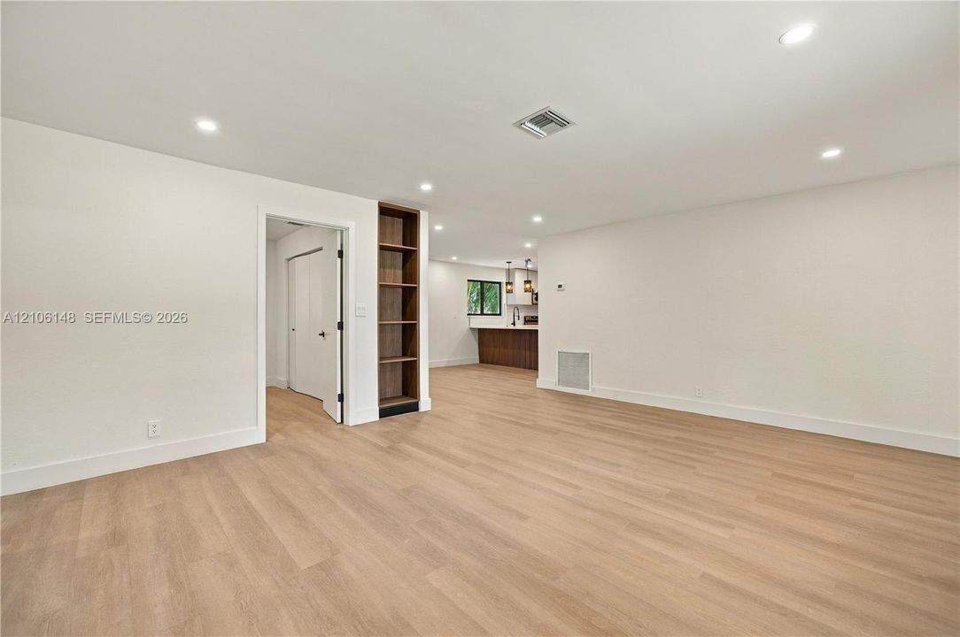 Open-concept interior featuring light wood-finish flooring, recessed lighting, and a built-in floor-to-ceiling shelving unit