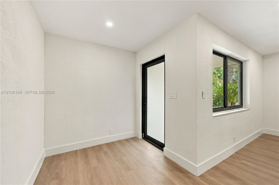 Interior space featuring wood-finish flooring, textured white walls, a black-framed glass exterior door, and a black-framed window