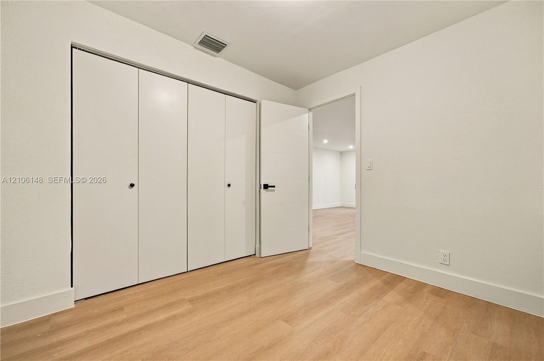 Room featuring light-toned wood-finish flooring, white walls, and a multi-panel closet with matte black hardware