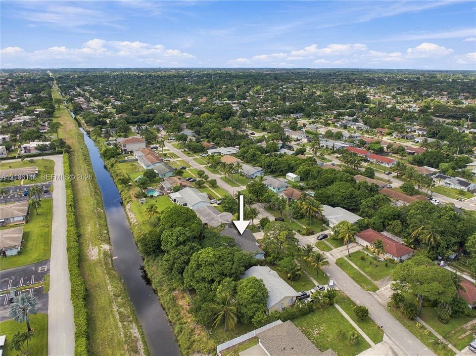 Aerial perspective of a property featuring mature perimeter trees, a canal-front position, and established neighborhood landscaping