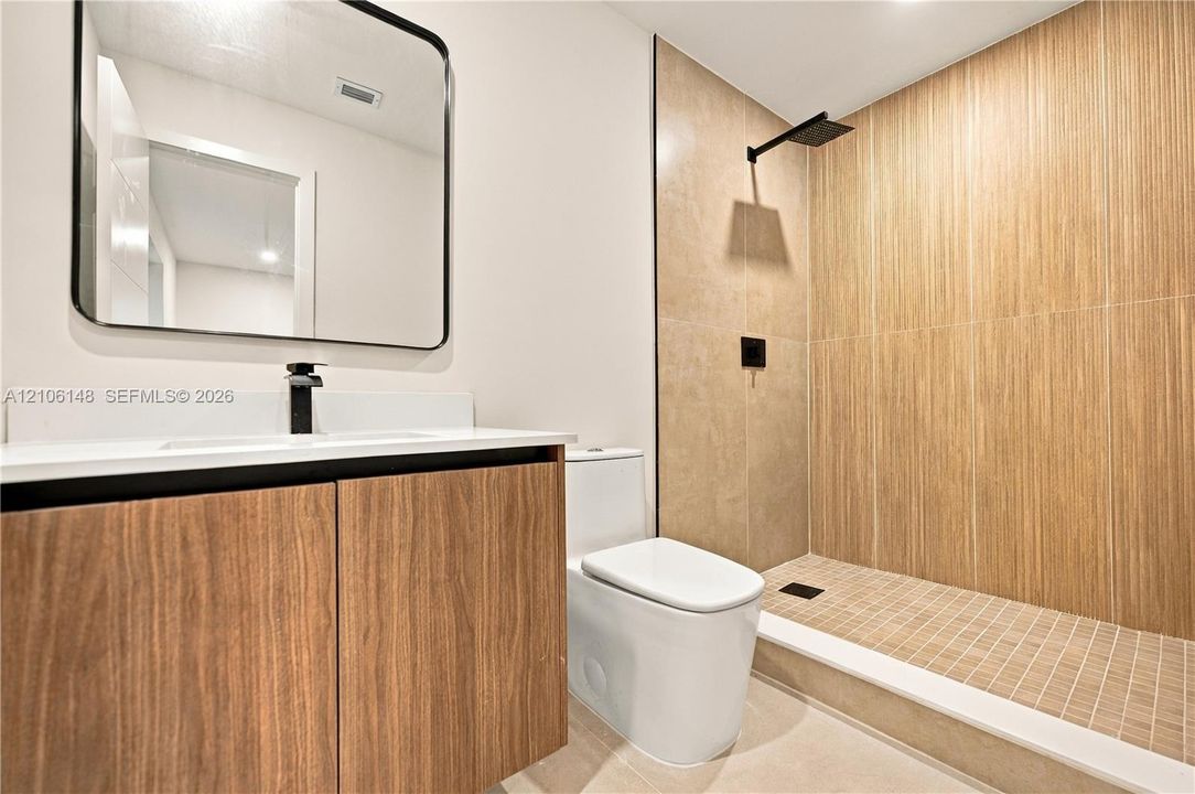 Bathroom featuring a wood-finish floating vanity, wall-mounted matte black faucet, rectangular mirror with a black frame, and a walk-in shower with vertical wood-texture tile and rain showerhead