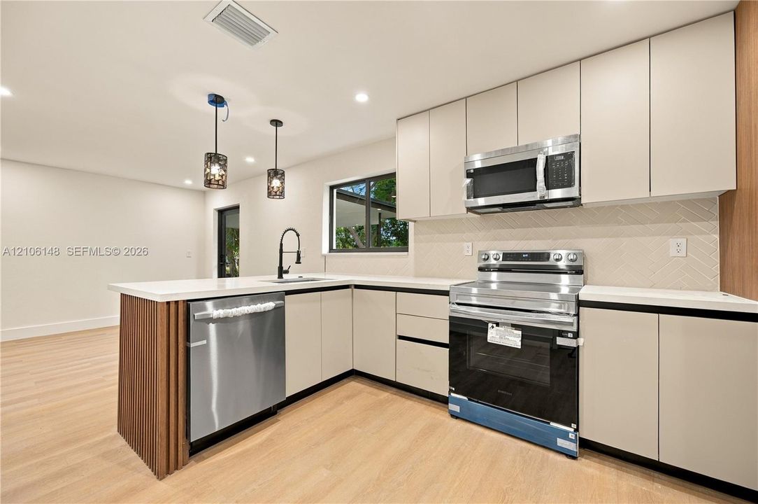 Kitchen featuring flat-panel cabinetry, quartz countertops, herringbone-pattern backsplash, stainless steel appliances, and wood-finish flooring