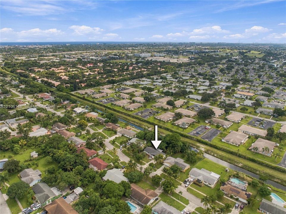Aerial perspective of a residential property featuring a pitched roof, attached garage, paved driveway, and mature landscaping within a suburban community