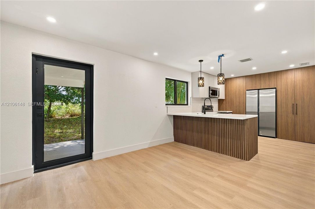 Kitchen featuring wood-finish cabinetry, a slatted island base, recessed lighting, integrated stainless steel appliances, and a glass-paneled exterior door
